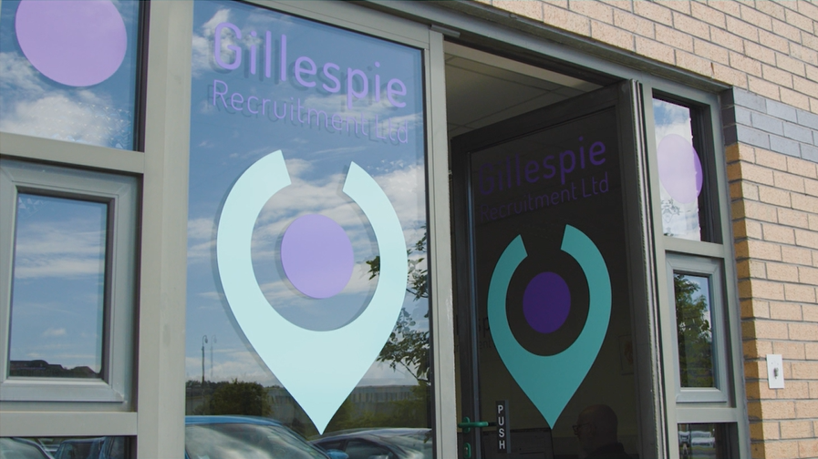 Picture of a door with a logo printed on. The logo is a location pin the is green and purple with Gillespie Recruitment printed above.